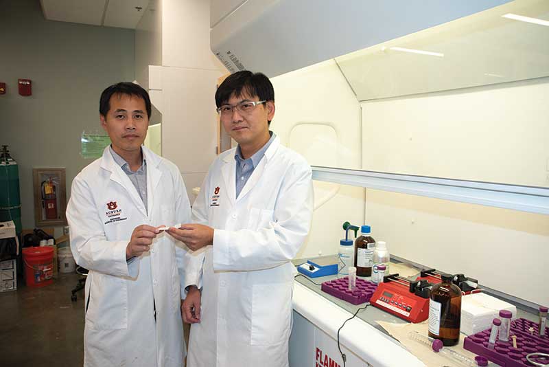 Two men wearing lab coats standing by lab equipment