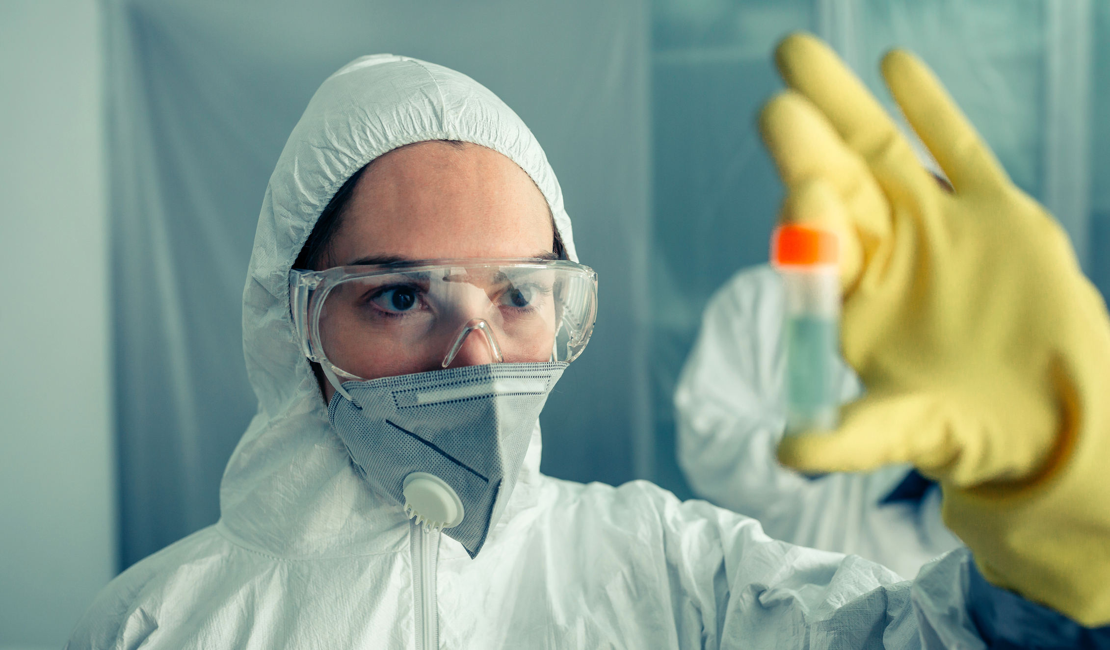 Researcher in a biosafety suit looking at a vial