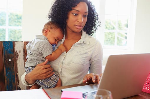 A woman holds a child while looking at a computer