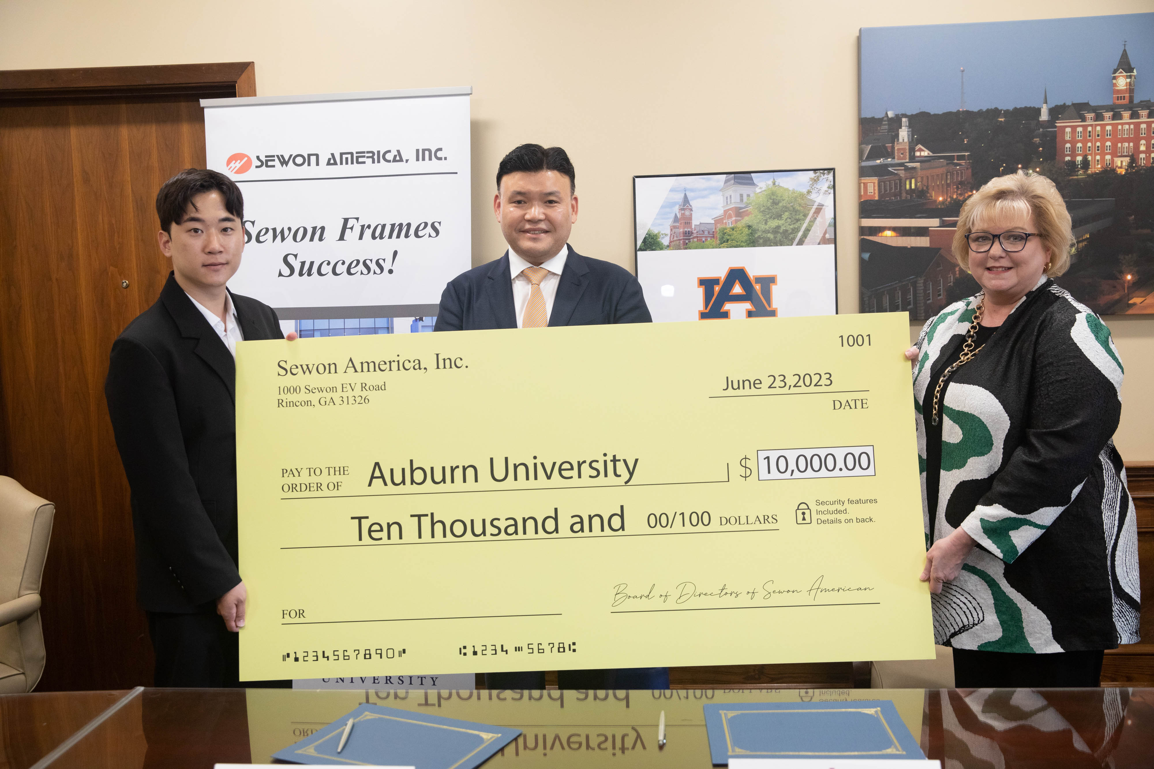Three people stand with a $10,000 check at a presentation.