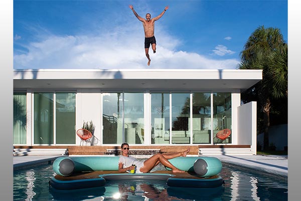 A man jumping into a pool and a woman floating holding a cup.