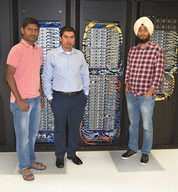 Three men stand in front of a supercomputer