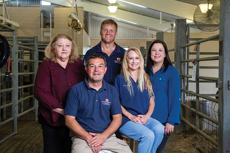 Five people pose while in an animal stable building