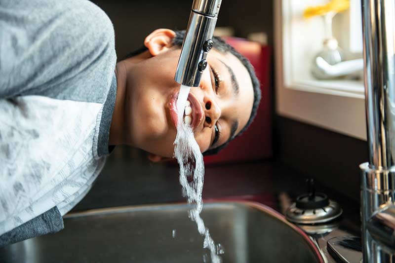 A young boy drinks from a faucet
